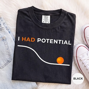 Peut inclure: Un t-shirt noir avec le texte blanc I HAD POTENTIAL, le mot HAD étant en orange. Sous le texte, une ligne blanche représente une pente descendante avec un cercle orange en bas. Le t-shirt porte une étiquette de col de marque Comfort Colors.