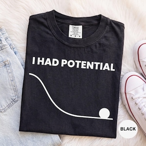 Peut inclure: Un t-shirt noir avec le texte blanc "I HAD POTENTIAL" au-dessus d'un graphique blanc représentant une courbe descendante se terminant par un cercle. Le t-shirt porte une étiquette Comfort Colors à l'intérieur du col indiquant une taille M.