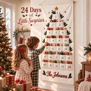 Op de afbeelding: Een cr&egrave;mekleurige stoffen adventskalender voor aan de muur in de vorm van een kerstboom met 24 genummerde vakjes met kleine cadeautjes. De tekst 24 Days of Little Surprises en The Johnsons is op de stof geborduurd met groene hulstaccenten.