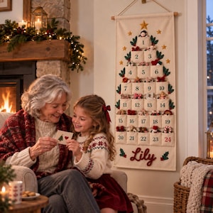 Op de afbeelding: Een cr&egrave;mekleurige stoffen adventskalender voor aan de muur in de vorm van een kerstboom met vierentwintig genummerde vakjes, groene vilten blaadjes, gouden sterren en de naam Lily in rood borduursel onderaan, opgehangen aan een houten stok.