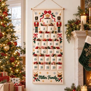 Peut inclure: Un calendrier de l'Avent mural en tissu crème avec vingt-quatre poches numérotées disposées en forme de sapin. Le motif comprend des casse-noisettes brodés, un nœud rouge, des flocons de neige et le texte Miller Family en bas.