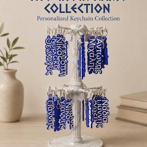 May include: A white marble-patterned rotating display stand holds multiple blue keychains with Greek names in white lettering. The text at the top reads THE GREEK NAME COLLECTION Personalized Keychain Collection. Two additional keychains lie below.