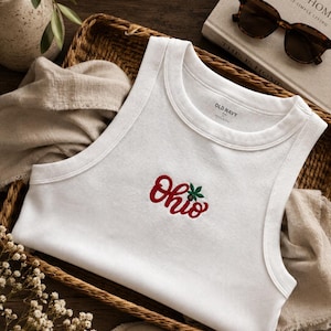 May include: A white ribbed tank top featuring an embroidered red script logo that reads Ohio, accented with a small green buckeye leaf design. The garment has a crew neckline and is labeled with Old Navy branding on the inner collar area.