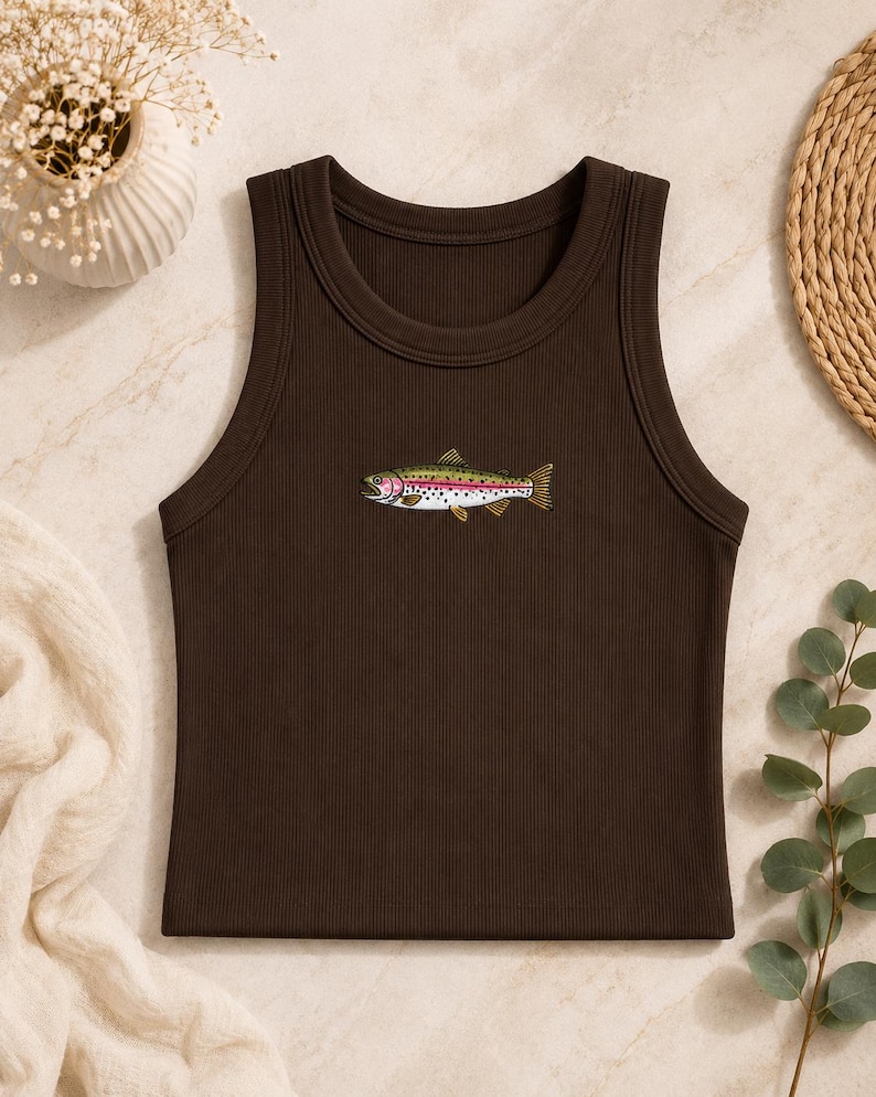 K&ouml;nnte beinhalten: Ein dunkelbraunes, geripptes Tanktop mit einer mittigen Stickerei einer Regenbogenforelle. Der Fisch ist mit einem gr&uuml;nen R&uuml;cken, einem rosa Seitenstreifen und schwarzen Punkten auf dem K&ouml;rper dargestellt. Das Kleidungsst&uuml;ck hat einen Rundhalsausschnitt.