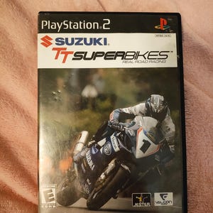 Puede incluir: Caja de videojuego de PlayStation 2 para Suzuki TT Superbikes. La portada muestra a un corredor de motos en acción. El título del juego y el logotipo de Suzuki son visibles. La clasificación ESRB está presente. NTSC U/C.