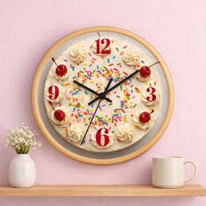 May include: A round wall clock designed to resemble a cake. The clock face features white frosting, colorful sprinkles, and red cherries. The numbers 3, 6, 9, and 12 are in red. The clock has a light brown wooden frame.