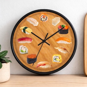 May include: A round wall clock with a black frame and a light brown wooden face. The clock face features various sushi pieces in place of numbers. Black clock hands indicate the time.
