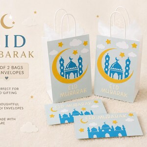 May include: Two light blue gift bags and two matching envelopes with a mosque and crescent moon design. The bags and envelopes have the words "Eid Mubarak" printed on them. The image also includes the text "Set of 2 bags & 2 envelopes".