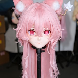 May include: A pink anime-style mask with long, flowing pink hair. The mask features large, red eyes and is adorned with fluffy pink ears with white accents. A white flower and branch detail is attached to one ear. The mask is mounted on a black stand.