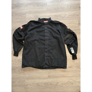 May include: Black racing jacket with a mandarin collar and long sleeves. The jacket features red and white patches on the sleeves and collar, and a vertical zipper closure. The cuffs are black and ribbed.