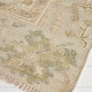 Puede incluir: Primer plano de una alfombra beige y marr&oacute;n claro con un aspecto envejecido y vintage. La alfombra presenta un estampado floral en tonos verdes, azules y rosas. El borde tiene un detalle de flecos. La alfombra est&aacute; hecha de un material tejido.