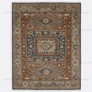 May include: Rectangular rug with a central geometric design in shades of brown and blue. The rug features a detailed border with floral and geometric patterns. The rug's design is symmetrical, with a central diamond shape and repeating motifs.