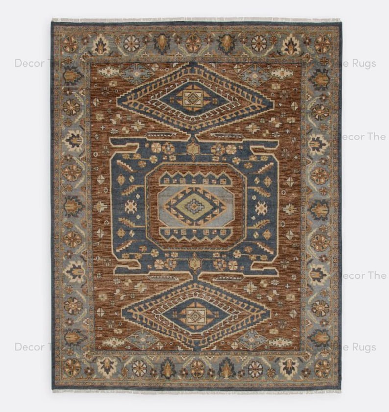May include: Rectangular rug with a central geometric design in shades of brown and blue. The rug features a detailed border with floral and geometric patterns. The rug's design is symmetrical, with a central diamond shape and repeating motifs.