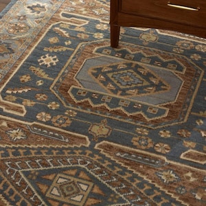 May include: A close-up of a blue and brown patterned rug with a geometric design. The rug features a central medallion and border with intricate floral and geometric motifs. A wooden cabinet leg is visible in the upper right corner.