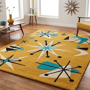 May include: Mustard yellow mid-century modern area rug with starburst and atomic designs in white, black, and teal. The rug is rectangular and placed on a wooden floor. The room also features a chair and a sofa.