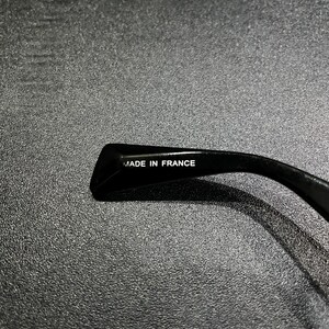 May include: A black temple arm of a pair of glasses featuring the text MADE IN FRANCE printed in white on the inner surface. The material has a smooth, glossy finish and a curved shape designed to rest behind the ear.