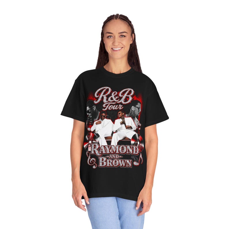 May include: A black short-sleeve t-shirt featuring a graphic print with the text R&B Tour Raymond and Brown. The design includes two figures in white suits, red circular accents, and stylized lettering in a glittery silver and red color scheme.