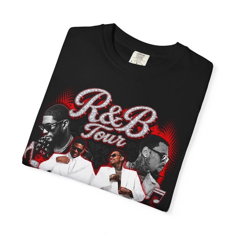 May include: A black t-shirt featuring a graphic print with the text R&B Tour in a diamond-like font. The design includes multiple images of a person wearing sunglasses and a white suit, set against a red and black background with musical notes.