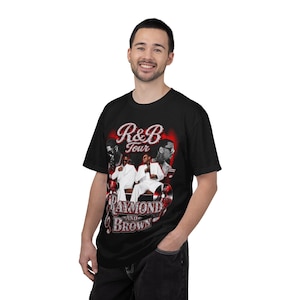 May include: A black short-sleeve t-shirt featuring a graphic print with the text R&B Tour and Raymond and Brown. The design includes images of two individuals in white suits, red accents, and musical elements like a treble clef and vinyl records.