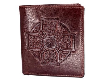 May include: A brown leather wallet featuring an embossed Celtic cross design. The cross is highly detailed with interwoven patterns. The wallet is rectangular and appears closed.