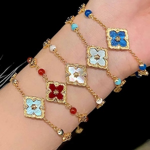 Pode incluir: Pulseiras douradas com pingentes em forma de trevo em várias cores: azul claro, vermelho, branco e azul escuro. Cada pingente é fixado em uma moldura dourada e conectado por uma delicada corrente dourada. Pequenas contas vermelhas, brancas e azuis.