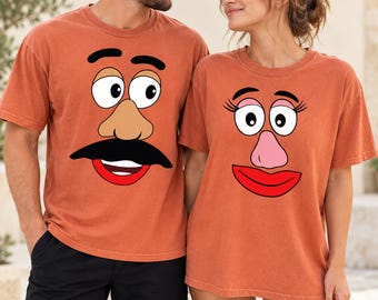 Könnte beinhalten: Zwei rostfarbene T-Shirts mit Rundhalsausschnitt und Cartoon-Gesichtsgrafiken. Ein Shirt zeigt eine Figur mit dicken schwarzen Augenbrauen, einer beigen Nase, einem schwarzen Schnurrbart und rotem Mund. Das andere zeigt Wimpern, eine rosa Nase und rote Lippen.