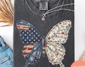 Könnte beinhalten: Dunkelgraues T-Shirt mit einem Schmetterlingsdesign. Ein Flügel zeigt die amerikanische Flagge, der andere ein Blumenmuster. Das T-Shirt hat einen Rundhalsausschnitt und kurze Ärmel. Der Text "SHIPS FAST!" ist sichtbar.
