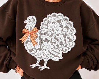 Könnte beinhalten: Ein dunkel schokoladenbraunes Sweatshirt mit Rundhalsausschnitt und einer großen weißen Grafik eines Truthahns, der aus komplizierten floralen Spitzenmustern besteht. Das Truthahnmotiv hat eine orange-weiß karierte Schleife.