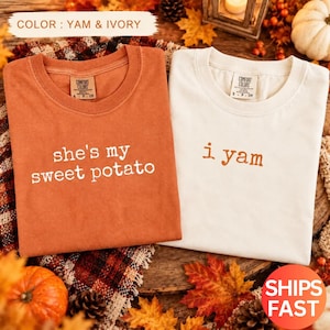 Puede incluir: Dos camisetas de cuello redondo, una de color naranja ñame y otra de color marfil. La camiseta naranja tiene el texto blanco "she's my sweet potato" y la de color marfil tiene el texto naranja "i yam". Ambas tienen una etiqueta Comfort Colors.