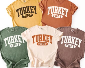 Könnte beinhalten: Fünf kurzärmelige T-Shirts mit Rundhalsausschnitt in Gelb, Orange, Grün, Creme und Braun. Jedes T-Shirt zeigt den Schriftzug TURKEY TROT in einer abgenutzten, gebogenen College-Schriftart auf der Brust in einer Kontrastfarbe.
