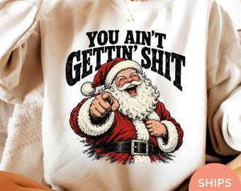 Könnte beinhalten: Ein sandfarbenes Sweatshirt mit Rundhalsausschnitt und einer Grafik eines lachenden, nach vorne zeigenden Weihnachtsmanns. Über der Illustration steht der Text YOU AIN'T GETTIN' SHIT in fetten, schwarzen, abgenutzten Buchstaben. Der Weihnachtsmann trägt einen roten Anzug.