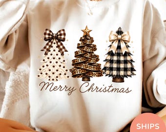 Könnte beinhalten: Ein sandfarbenes Sweatshirt mit Rundhalsausschnitt und einer Grafik von drei stilisierten Weihnachtsbäumen. Der linke Baum hat eine schwarz-weiß karierte Schleife, der mittlere ein Leopardenmuster-Band und der rechte eine beigefarbene Schleife. Darunter steht der Text Merry Christmas.
