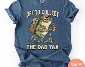 Könnte beinhalten: Denimblaues T-Shirt mit einem Cartoon-Frosch auf einem Roller, der eine Kappe und eine Brille trägt und einen Rucksack und ein Getränk trägt. Der Text lautet "OFF TO COLLECT THE DAD TAX".