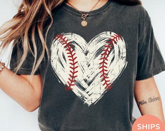Könnte beinhalten: Dunkelgraues T-Shirt mit einem verblichenen weißen Herzdesign und roten Baseballnähten. Das Shirt hat einen Vintage-Look. Der Text "SHIPS FAST!" ist unten rechts sichtbar.