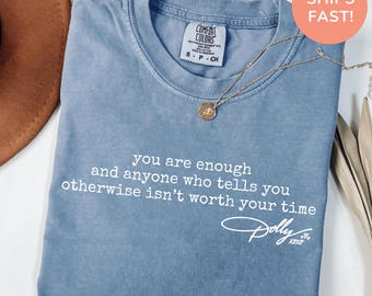 Könnte beinhalten: Ein blaues T-Shirt in Jeansoptik mit Rundhalsausschnitt und kurzen Ärmeln. Das Shirt zeigt weißen Text mit der Aufschrift, you are enough and anyone who tells you otherwise isn't worth your time, gefolgt von einer Unterschrift, Dolly xoxo.