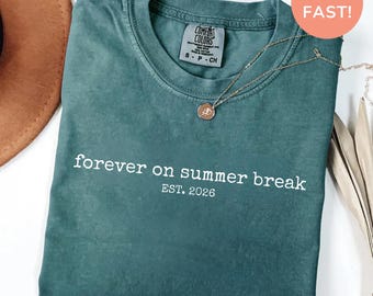 Könnte beinhalten: Blau-Fichte Comfort Colors T-Shirt mit dem Text "forever on summer break EST. 2026" in Weiß. Eine goldene Halskette mit Anhänger liegt über dem Shirt. Das Shirt hat einen Rundhalsausschnitt.