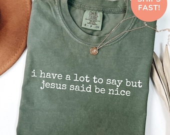 Könnte beinhalten: Ein moosgrünes Kurzarm-T-Shirt mit dem weißen Aufdruck "i have a lot to say but jesus said be nice" auf der Brust. Das T-Shirt hat einen Rundhalsausschnitt und ein Comfort Colors Markenetikett im inneren Kragenbereich.