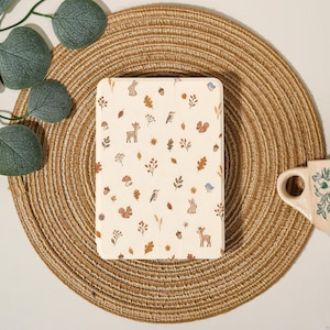 May include: A rectangular off-white tablet case featuring a repeating pattern of small woodland creatures including deer, rabbits, and squirrels, interspersed with autumn leaves, acorns, mushrooms, and wildflowers in muted earth tones.