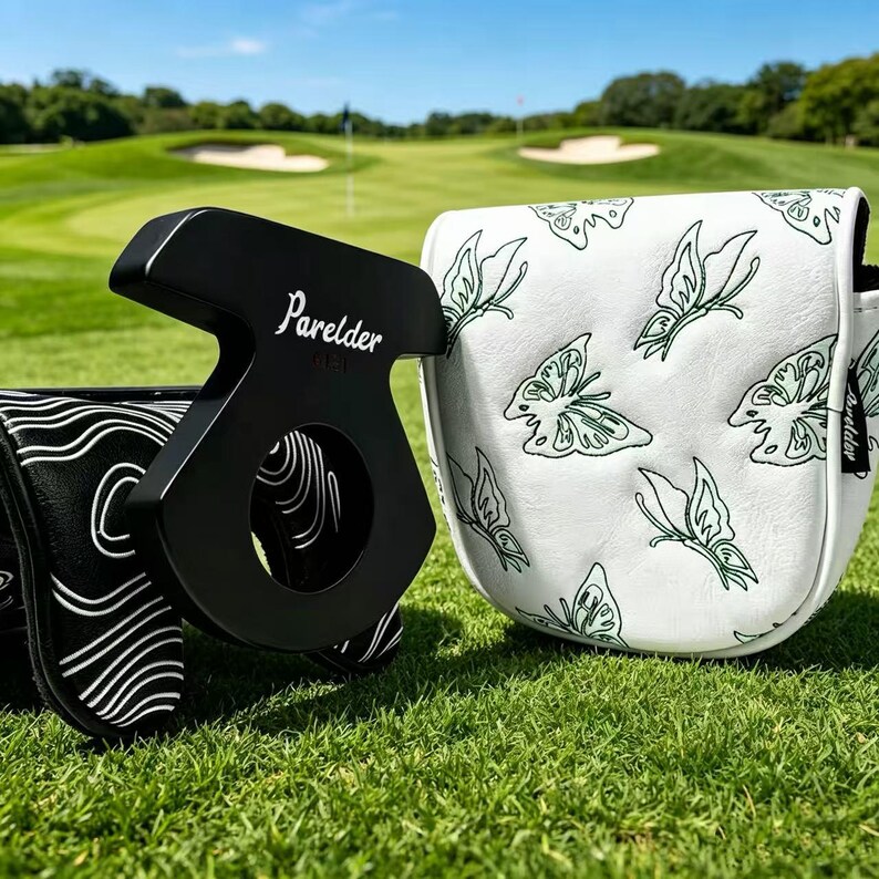 May include: A black putter head cover with white wavy lines and a white putter head cover featuring a green butterfly pattern. Both covers display the brand name Parelder in white text. The items are positioned on a green golf course fairway.