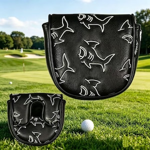 May include: A black golf putter headcover featuring a white shark pattern and a small side tag. The cover has a textured surface and a U-shaped opening on the bottom piece. The design includes multiple shark outlines across the exterior surface.