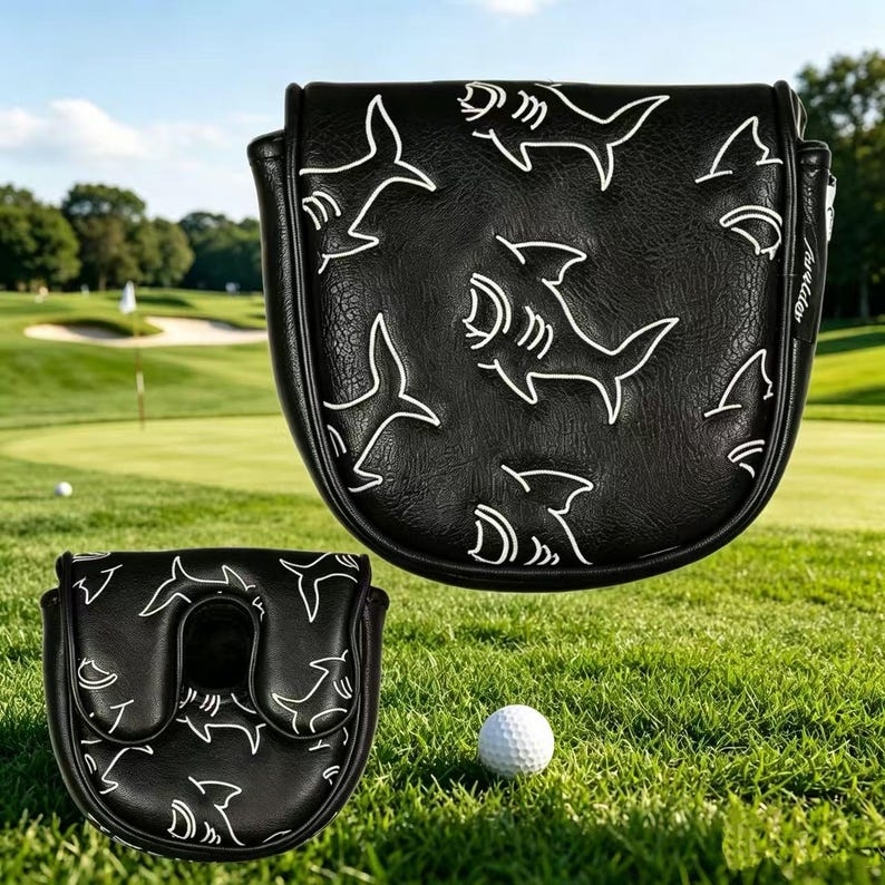 May include: A black golf putter headcover featuring a white shark pattern and a small side tag. The cover has a textured surface and a U-shaped opening on the bottom piece. The design includes multiple shark outlines across the exterior surface.