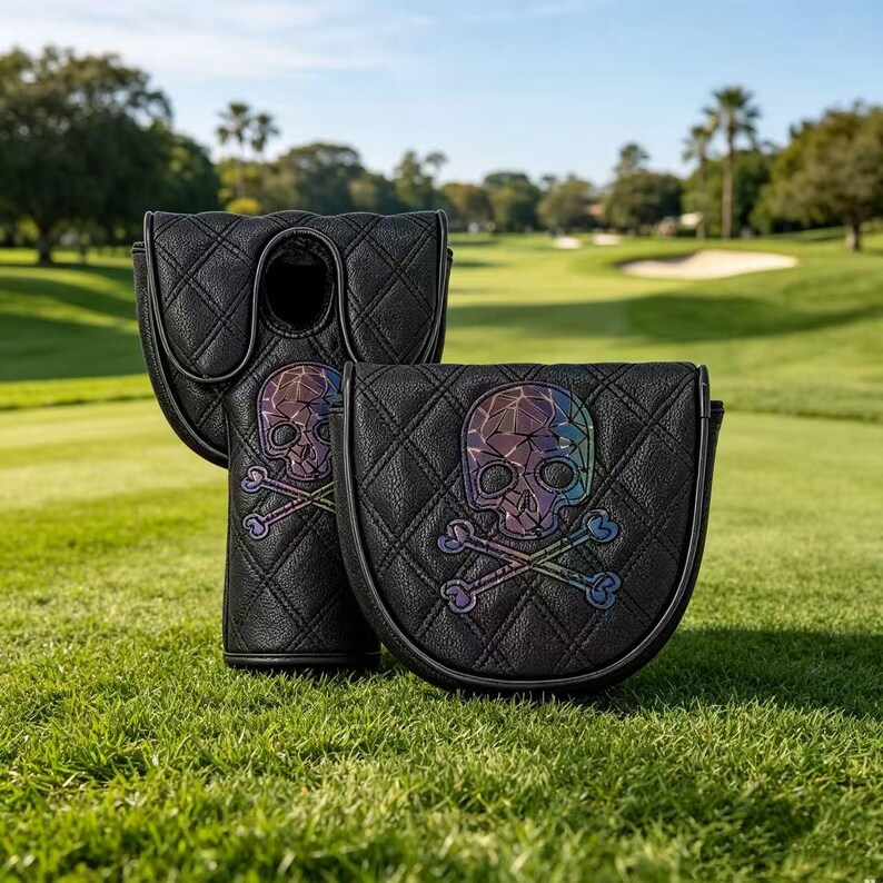 Puede incluir: Dos fundas negras para putter de golf con un patr&oacute;n de diamantes acolchado y un gr&aacute;fico central iridiscente de calavera y tibias cruzadas. Las fundas est&aacute;n hechas de un material texturizado con ribetes negros en los bordes y forma estructurada.