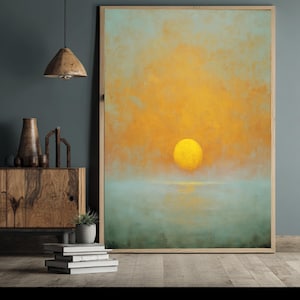 May include: A large rectangular framed wall art piece featuring an abstract painting of a bright yellow sun centred against a hazy orange sky above a calm, muted teal horizon line. The artwork is displayed in a light-coloured wooden frame.