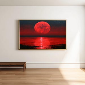 May include: A rectangular wall art print featuring a large, textured red moon centered in a dark sky above a calm body of water. The moon casts a bright, vertical red reflection across the water's surface, framed by a thin gold-colored border.