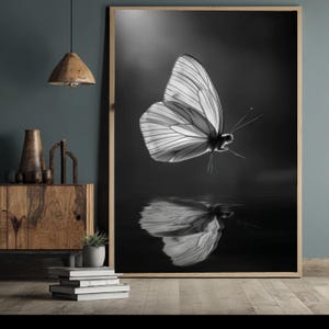 May include: A large rectangular framed wall art piece featuring a black and white photograph of a butterfly in flight above a dark, reflective surface. The butterfly is positioned in the upper center, with its wings spread and a clear reflection below.