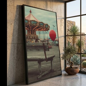 May include: Framed photograph of a carousel with a red and white striped roof and a red balloon floating in the foreground. A wooden bench sits on a boardwalk. The image is displayed in a black frame.
