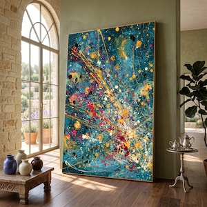 Puede incluir: Gran pintura abstracta con un fondo turquesa y vibrantes salpicaduras de amarillo, rojo y negro. La obra de arte está enmarcada en un tono de madera natural y se apoya contra una pared en una habitación bien iluminada.
