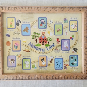 May include: A framed print with a light wood ruler-style frame. The print features a schoolhouse, a winding road, and illustrations representing grades 1st through 12th. The words "Memory Lane" are in the center of the print.