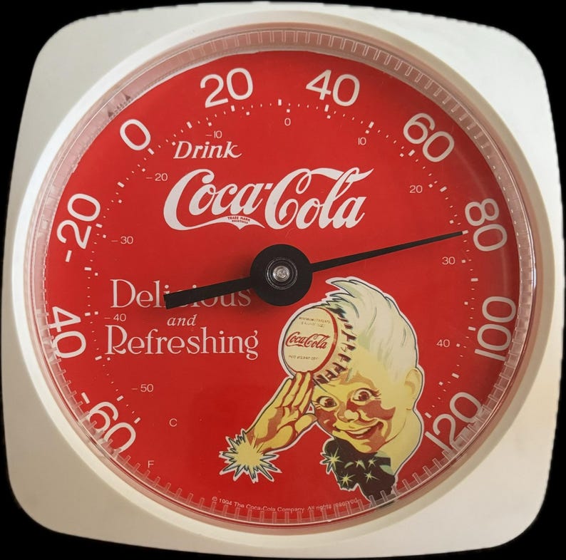 May include: A round Coca-Cola thermometer with a white frame and a red face. The dial features the text Drink Coca-Cola, Delicious and Refreshing, and a graphic of a person holding a bottle cap. It displays temperature in Fahrenheit and Celsius.