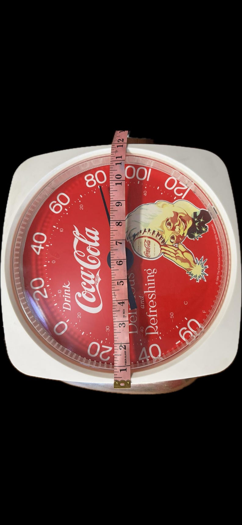 May include: A white analog scale with a red circular face featuring Coca-Cola branding, a vintage illustration of a person, and the text Drink Coca-Cola and Delicious and Refreshing. A measuring tape shows the scale face is approximately 11 inches wide.